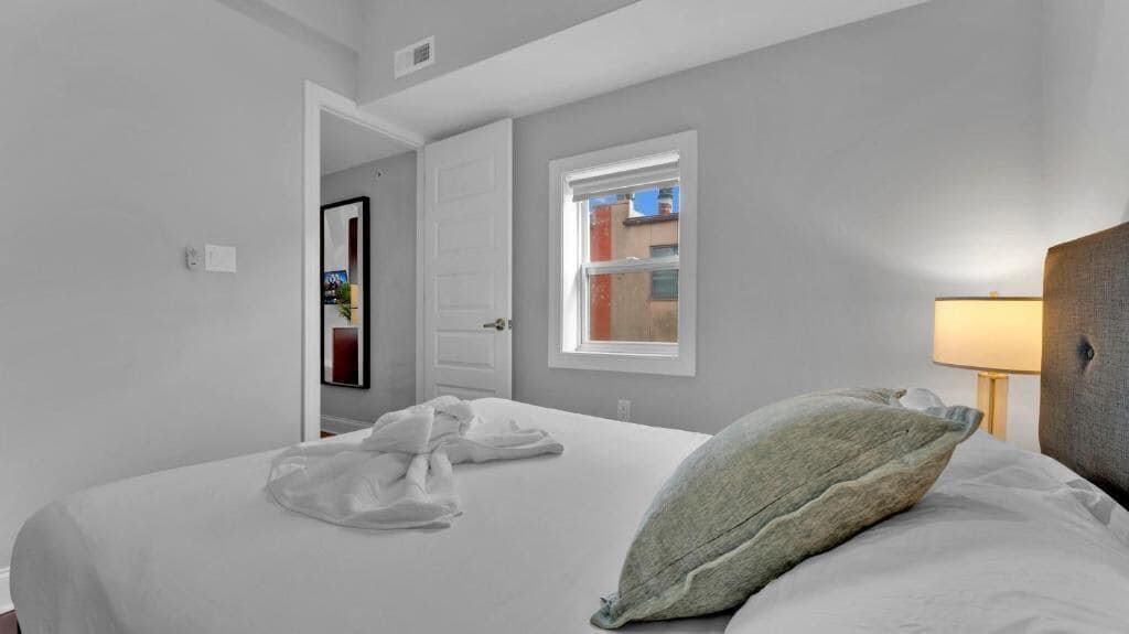 Une chambre d’hôtel avec un lit, une fenêtre, une lampe et une porte.