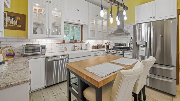 A modern kitchen with white cabinets, stainless steel appliances, and a wooden dining table. - Charming & Updated 1867 Brick House in Historic Downtown Delaware, OH; Sleeps 12 (Delaware)