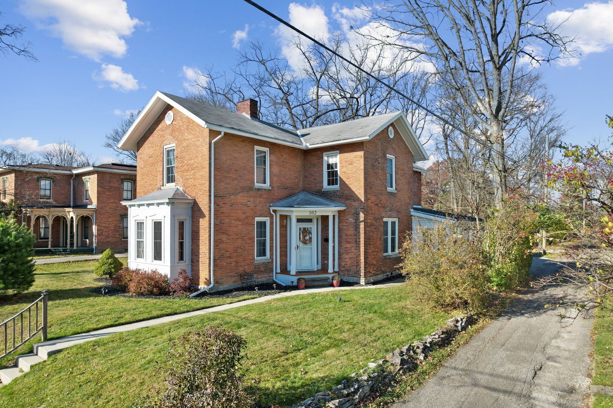 A two-story brick house with a front porch, a small attached garage, and a well-maintained lawn.