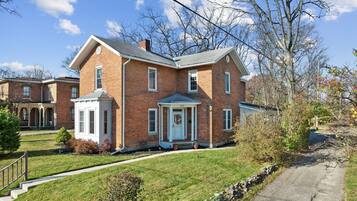 A two-story brick house with a front porch, a small attached garage, and a well-maintained lawn.