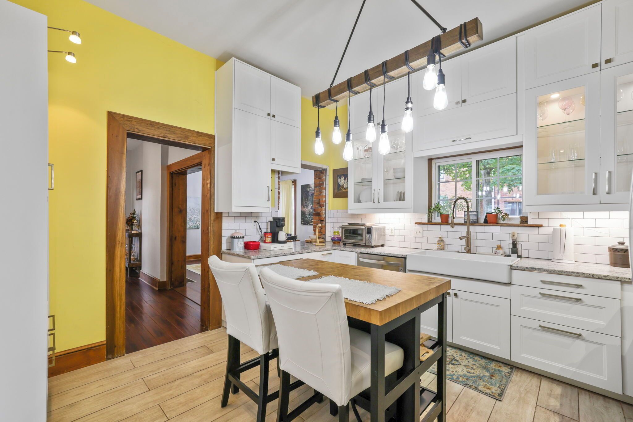 A modern kitchen with white cabinets, a wooden dining table, and pendant lighting.