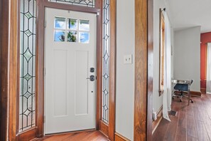 A white door with a glass panel and a metal grille, wooden floor, and a metal cart in the hallway. - Charming & Updated 1867 Brick House in Historic Downtown Delaware, OH; Sleeps 12 (Delaware)