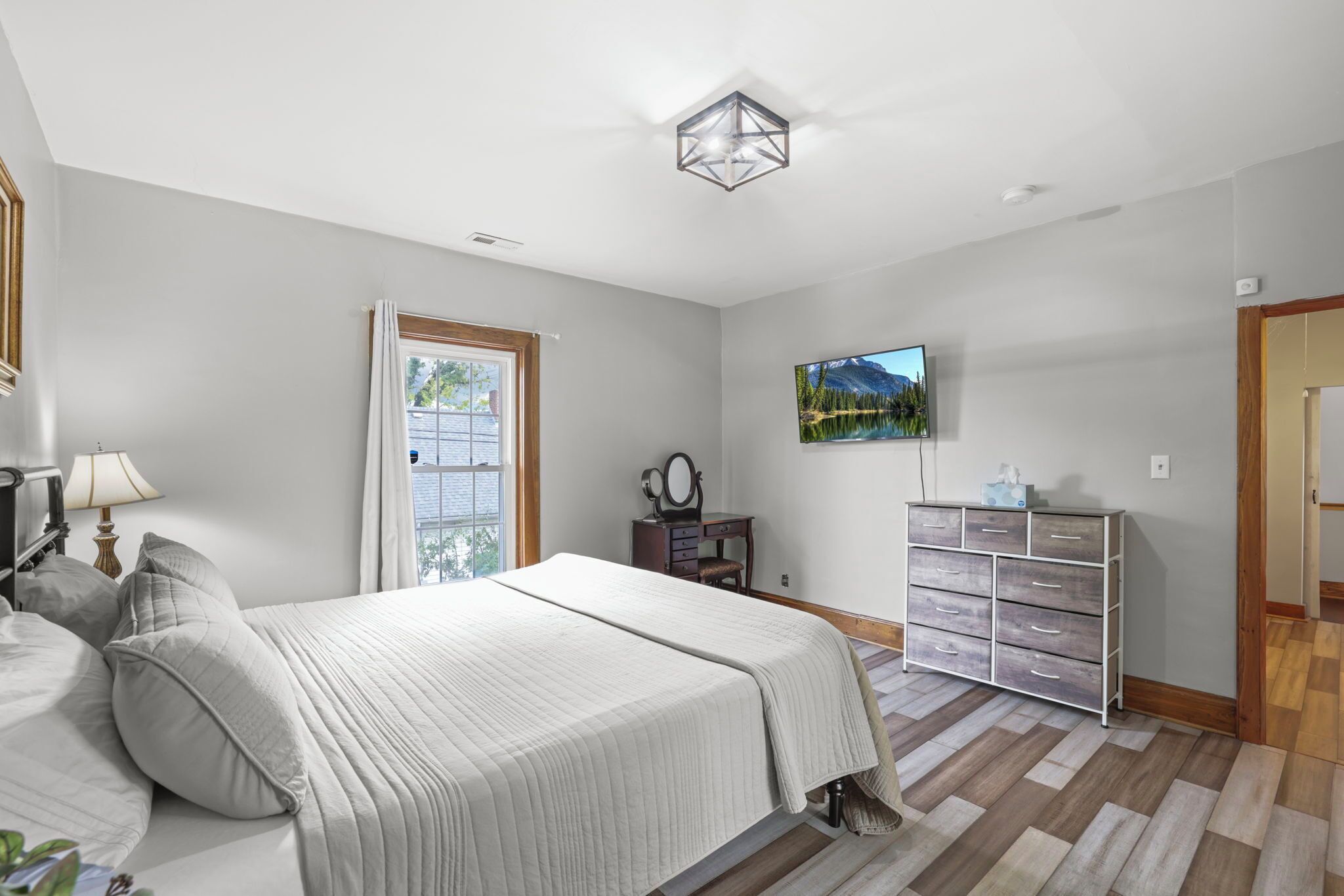 A bedroom with a bed, a dresser, a television, and a window with curtains.