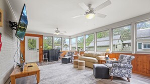 A spacious living room with a large window, a ceiling fan, and a flat-screen TV mounted on the wall. - Charming & Updated 1867 Brick House in Historic Downtown Delaware, OH; Sleeps 12 (Delaware)