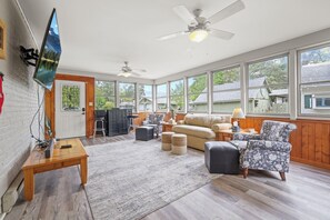 A spacious living room with a large window, a ceiling fan, and a flat-screen TV mounted on the wall. - Charming & Updated 1867 Brick House in Historic Downtown Delaware, OH; Sleeps 12 (Delaware)