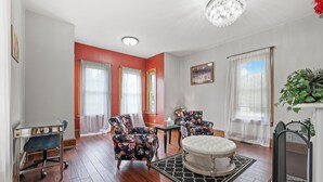 A living room with a fireplace, two armchairs, a round ottoman, a glass coffee table, and a desk with a chair. - Charming & Updated 1867 Brick House in Historic Downtown Delaware, OH; Sleeps 12 (Delaware)