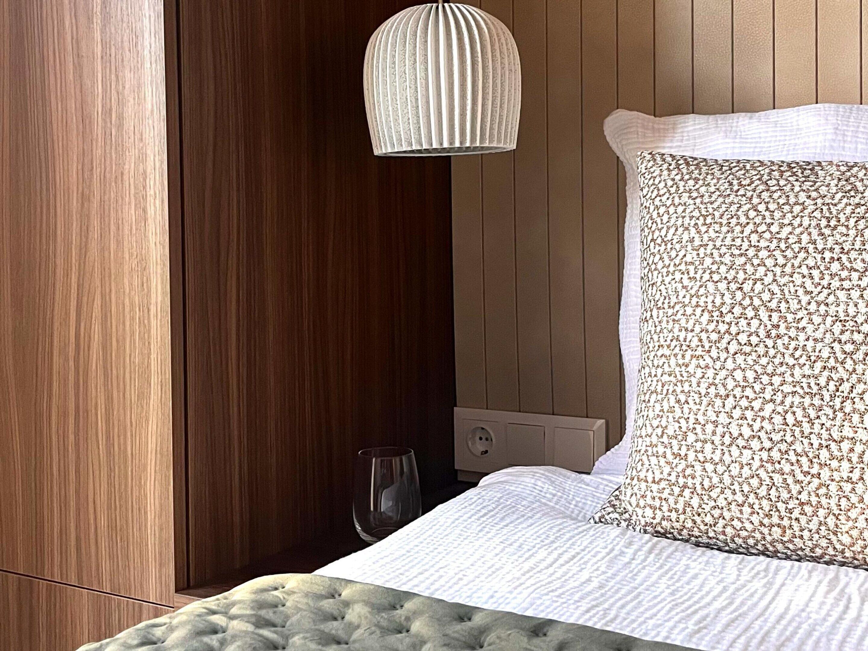 Une chambre avec un mur recouvert de panneaux de bois, une tête de lit capitonnée, un coussin à motifs et un luminaire suspendu à nervures.