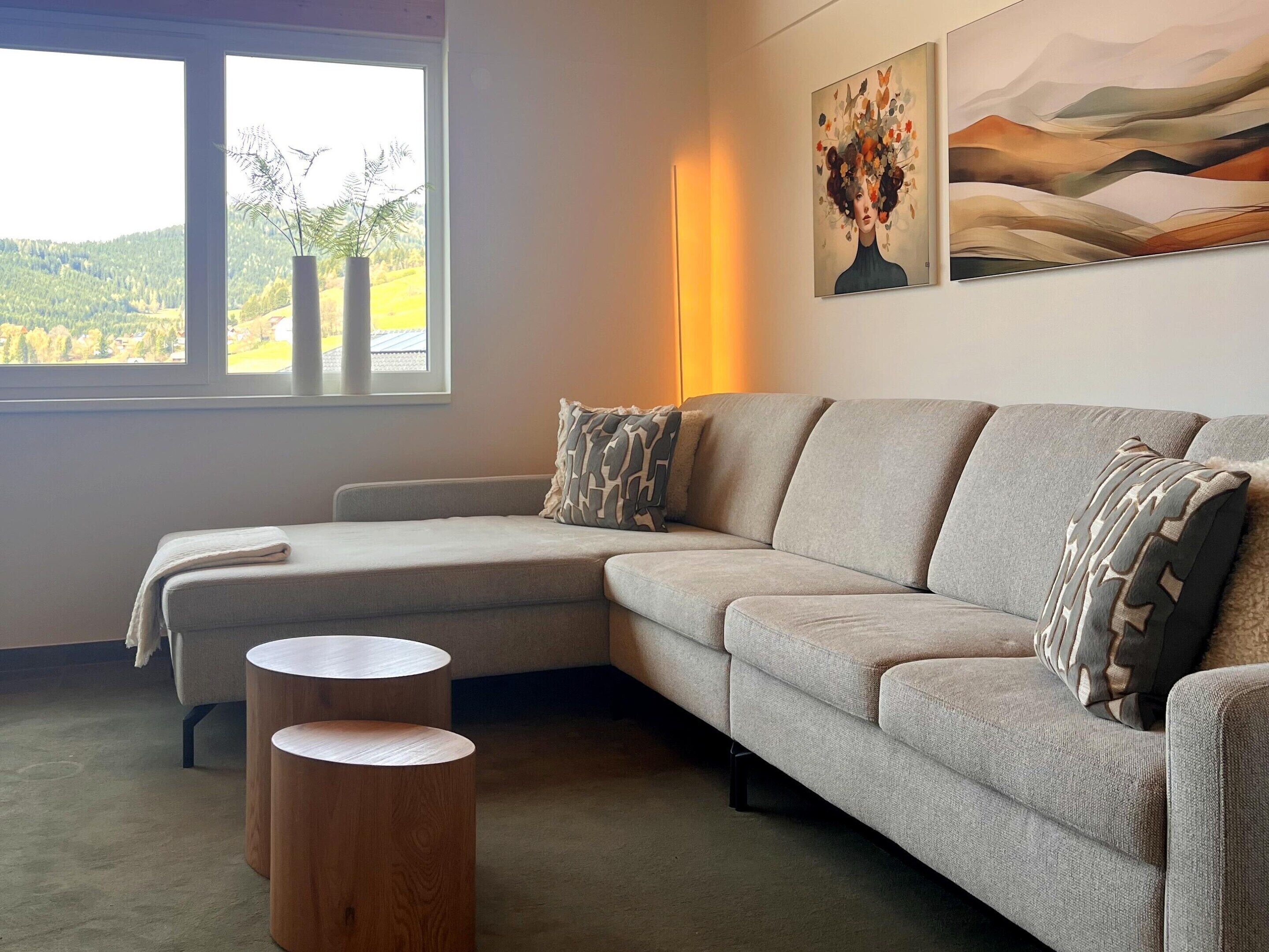 Una sala moderna con un sofá seccional, una pequeña mesa auxiliar de madera y vistas a un paisaje verde a través de una ventana.