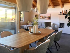 Un comedor moderno con una mesa de madera, sillas tapizadas en gris, un florero con flores e iluminación colgante.