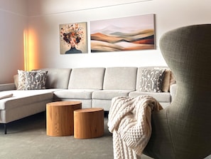 Ein modernes Wohnzimmer mit einer Eckcouch, zwei Holztischen und einem großen Sessel.