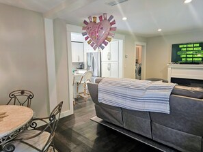 A living room with a sofa, a dining table with chairs, a kitchen in the background, and a TV displaying text. - Perfect 2-bedroom house with AC in quaint Decatur (Decatur)
