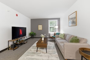 Ein Wohnzimmer mit Fernseher, Couchtisch, Sofa und Fenster.