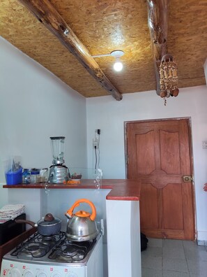 Eine Küche mit Gasherd, Mixer und Wasserkocher. Die Decke und die Tür sind aus Holz.
