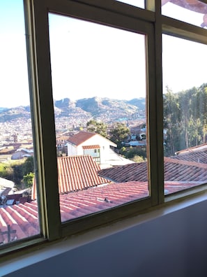 Blick durch ein Fenster auf eine Stadtansicht mit roten Ziegeldächern, einer Kirche und fernen Bergen.