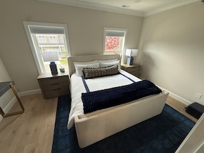 Une chambre à coucher avec un lit, des tables de chevet, une commode, une fenêtre et une vue sur l’extérieur.