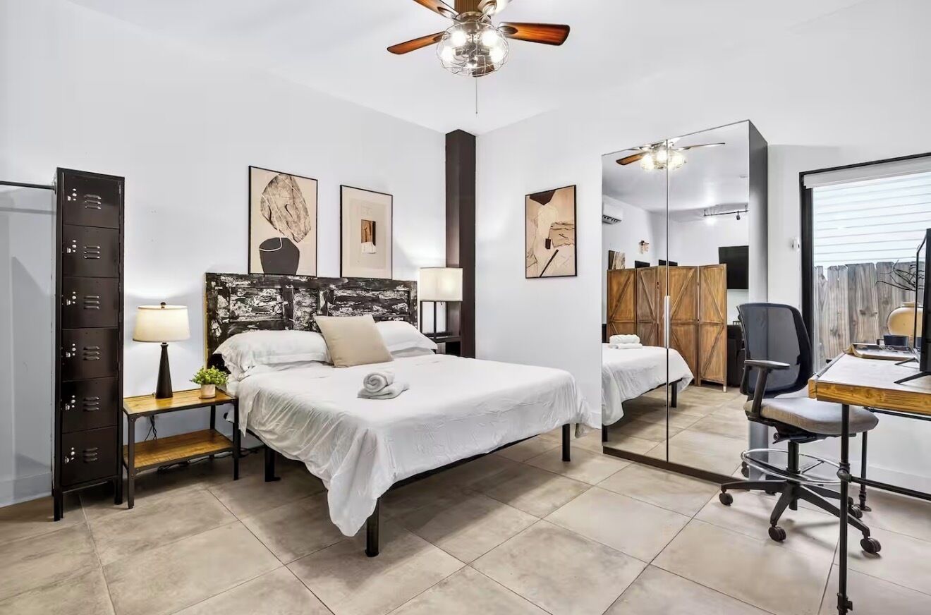 Une chambre d’hôtel comprenant un lit, des tables de chevet, un bureau, une chaise, un ventilateur de plafond et des œuvres d’art accrochées aux murs.