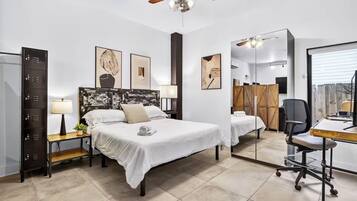 Une chambre d’hôtel comprenant un lit, des tables de chevet, un bureau, une chaise, un ventilateur de plafond et des œuvres d’art accrochées aux murs.