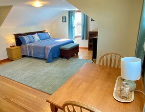 A bedroom with a bed, bedside table, lamp, and a view of the outside.