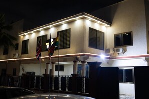 Un edificio con iluminación exterior, varias banderas y una entrada porticada.