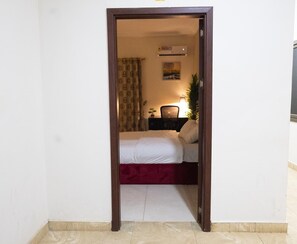 Un dormitorio con cama, escritorio, silla, planta en maceta y aire acondicionado instalado en la pared.