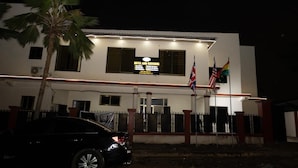 Un hôtel avec une enseigne indiquant qu’il propose des services d’hôtellerie et de restauration, un mât avec plusieurs drapeaux, et une voiture garée devant.