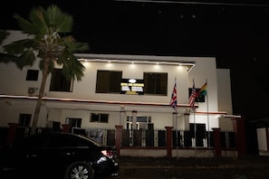 A hotel with a signboard indicating hotel and catering services, a flagpole with multiple flags, and a parked car in front.