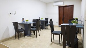 A dining area with tables and chairs, an air conditioning unit, and a ceiling fan. - Maya Lodge (Accra)
