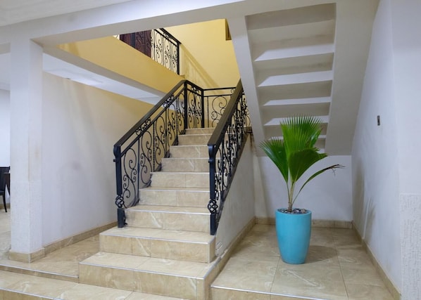 Una escalera con barandilla de hierro forjado negro, una planta en maceta y piso de baldosas.
