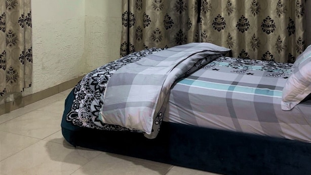 A bedroom with a bed, curtains, a ceiling fan, and a mounted television.