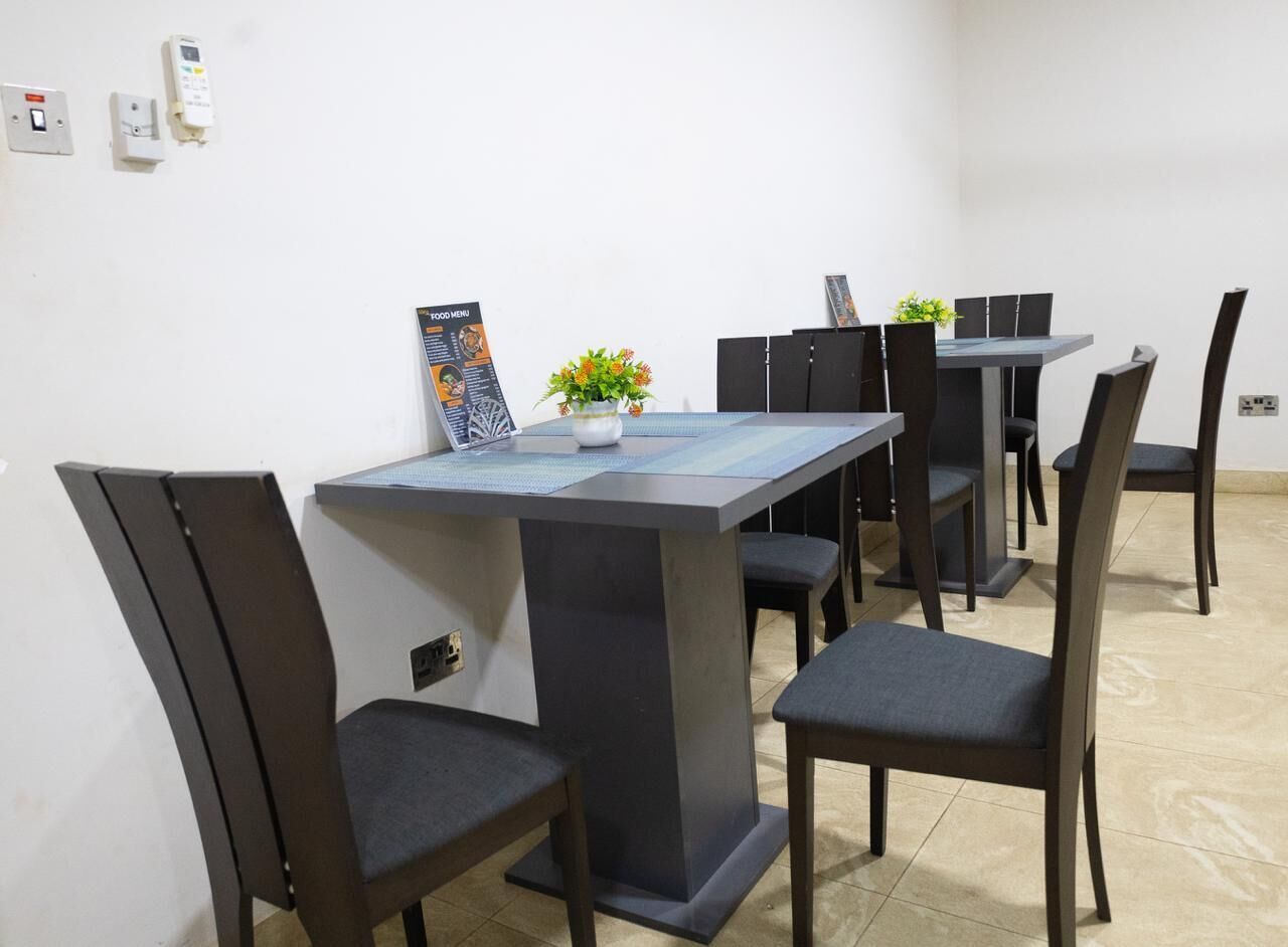 Un comedor con una mesa rectangular, seis sillas, un jarrón pequeño con flores y un cartel con el menú de comida en la pared.