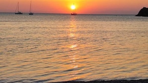 Solnedgang over et roligt hav med både og en klippefyldt kystlinje.
