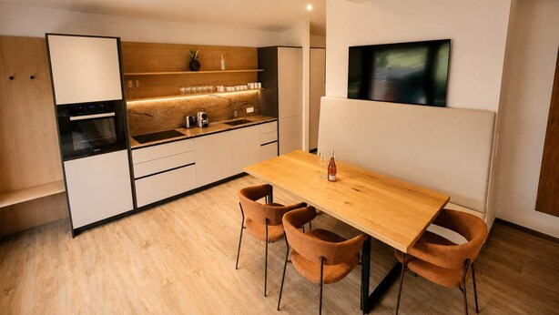 Una cocina moderna con encimera de madera, horno empotrado y zona de comedor con mesa de madera y cuatro sillas.