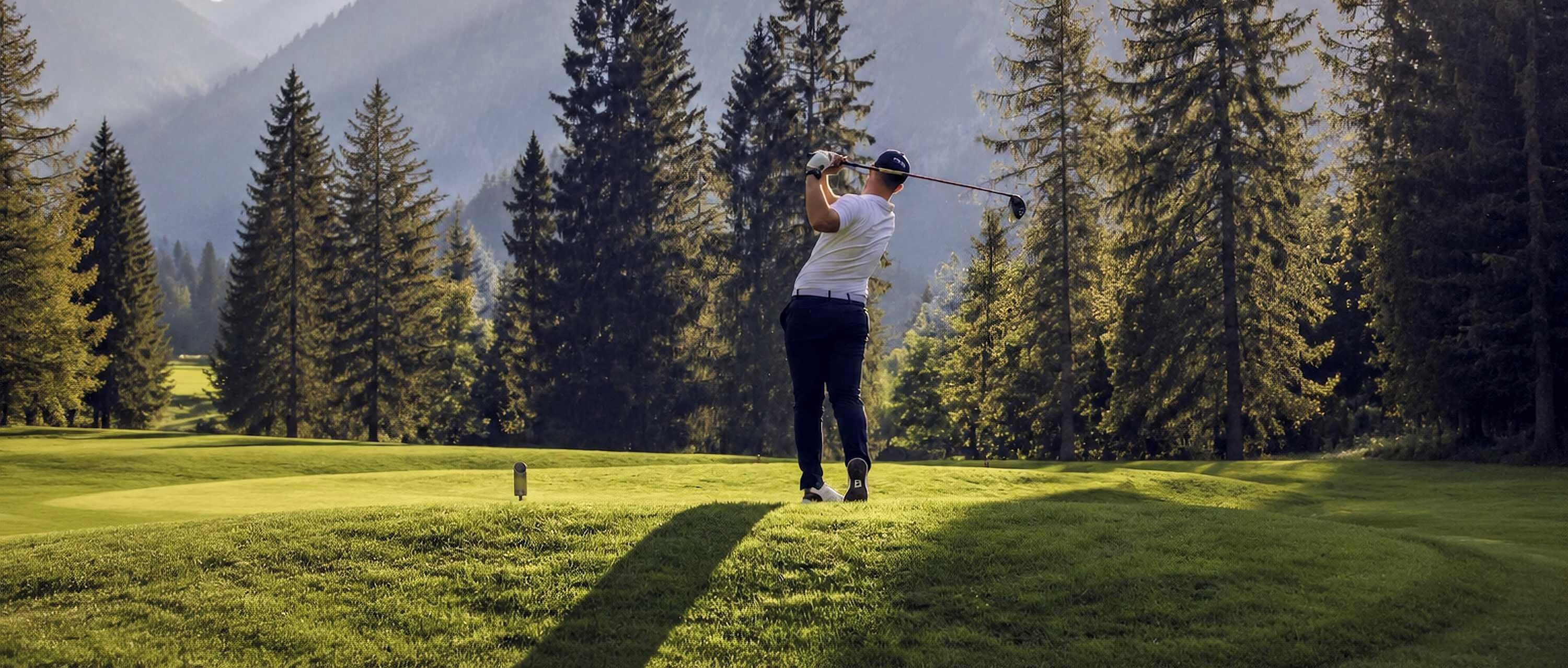 Eine Person spielt Golf auf einem Platz, mit hoch aufragenden Bäumen und Bergen im Hintergrund.