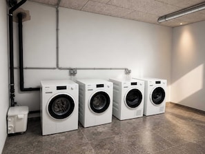 A laundry room with three white front-loading washing machines, a white utility sink, and a grey tiled floor. - BASE Achensee Soul N°37 (Achenkirch)