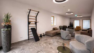 Un espace de détente moderne avec un sol en pierre, des canapés gris, un mur d’escalade en bois et une grande plante en pot.