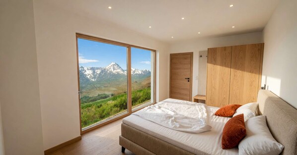 A bedroom with a large sliding glass door, a bed with pillows, and a wooden wardrobe. - BASE Achensee Soul No7 – Private hot tub (Achenkirch)