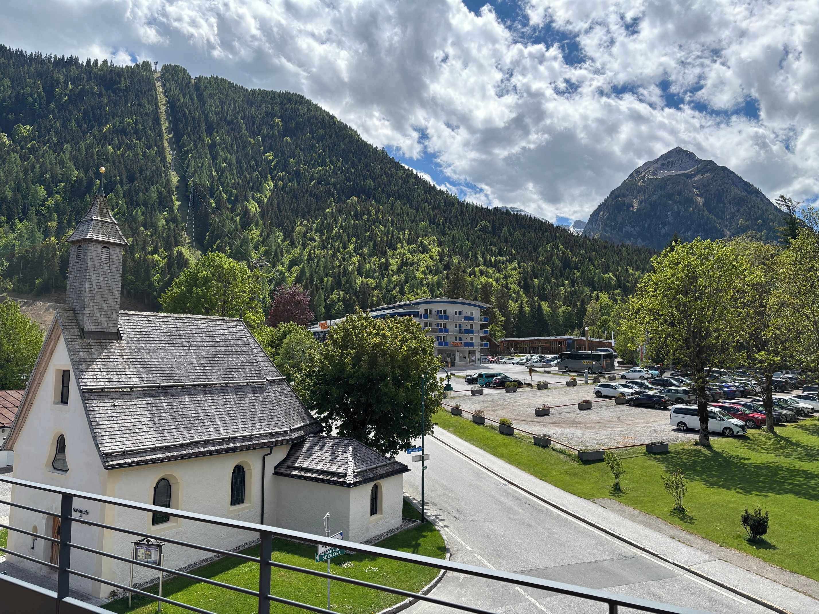 A church with a bell tower, a parking lot, and a mountain in the background.