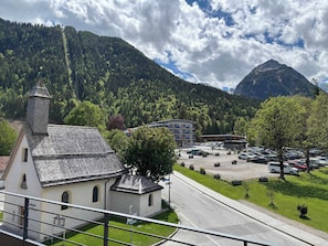 A church with a bell tower, a parking lot, and a mountain in the background.