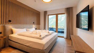 Ein Hotelzimmer mit einem großen Bett, einem Flachbildfernseher, einem Holz-Kopfteil, einem Balkon mit Bergblick und einem kleinen Tisch.