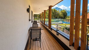 Uma varanda com piso de madeira, uma mesa e cadeiras, com vista para uma paisagem montanhosa e uma quadra de tênis.