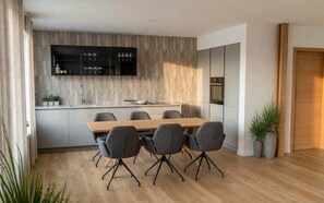 A modern kitchen with a wooden countertop, built-in cabinets, and a dining area with a wooden table and grey chairs.