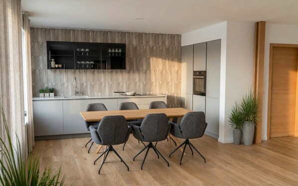 A modern kitchen with a wooden countertop, built-in cabinets, and a dining area with a wooden table and grey chairs.