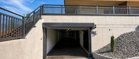 A modern building entrance with a concrete ramp, metal railings, and a gravel area with a small tree.