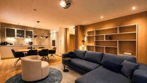 Een moderne woonkamer met een hoekbank, een rond voetenbankje en een eethoek met een houten tafel en stoelen.