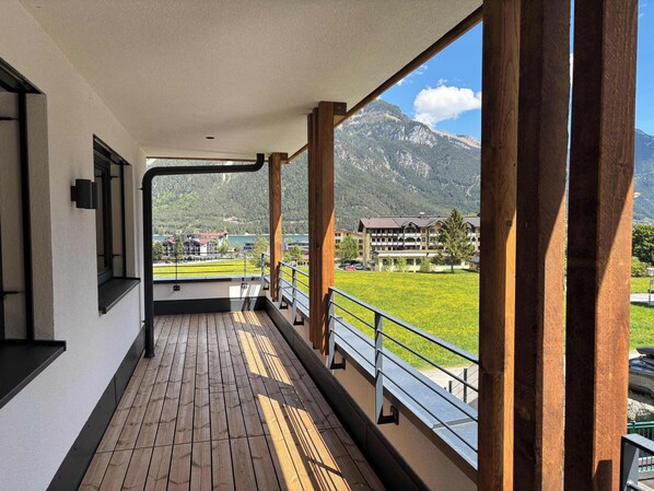 A balcony with a wooden floor, a metal railing, and a view of a mountain and buildings.