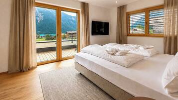 Quarto de hotel com cama, televisão de tela plana, varanda com vista para as montanhas e piso de madeira.