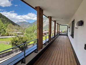 Un balcón cubierto con vigas de madera, baranda de metal y vista a un paisaje montañoso.