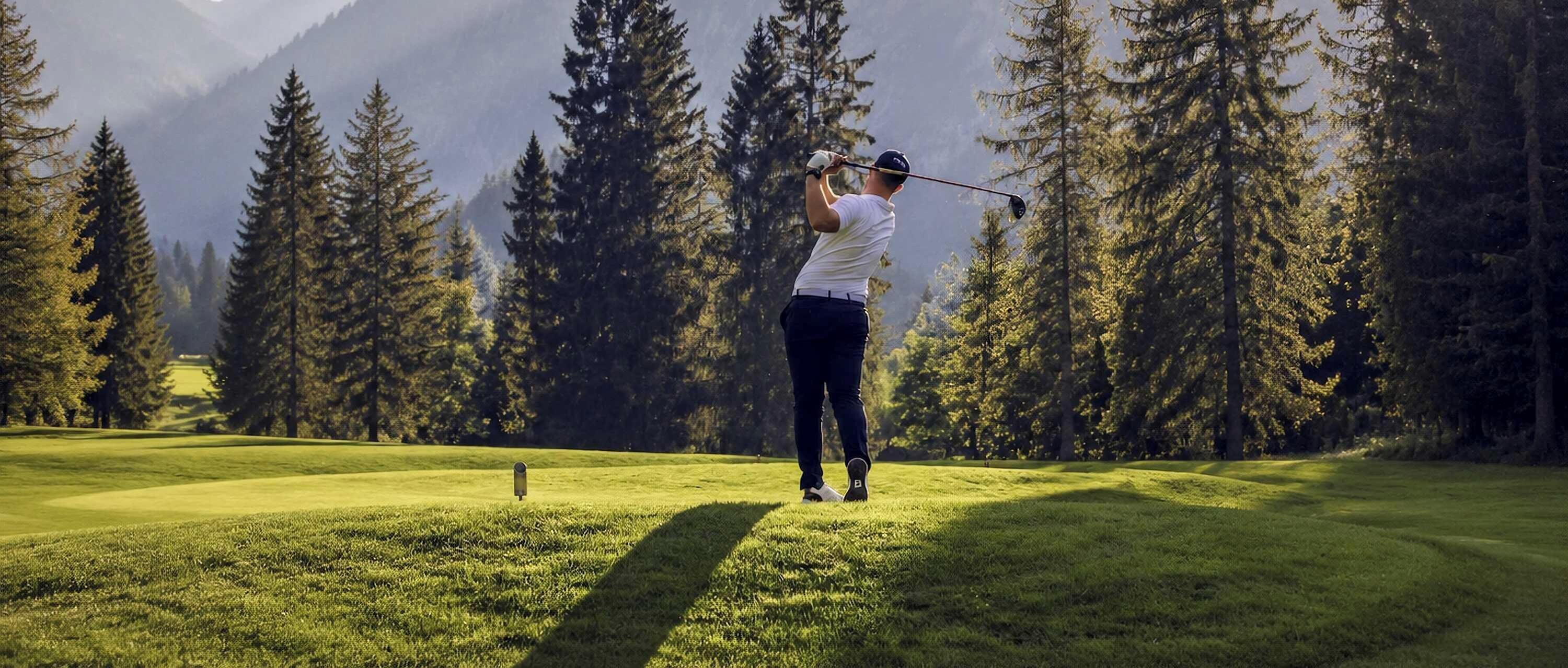 Eine Person spielt Golf auf einem Platz, mit hoch aufragenden Bäumen und Bergen im Hintergrund.