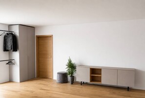 A minimalist room with a wardrobe, a grey ottoman, a potted plant, and a light-colored console table.