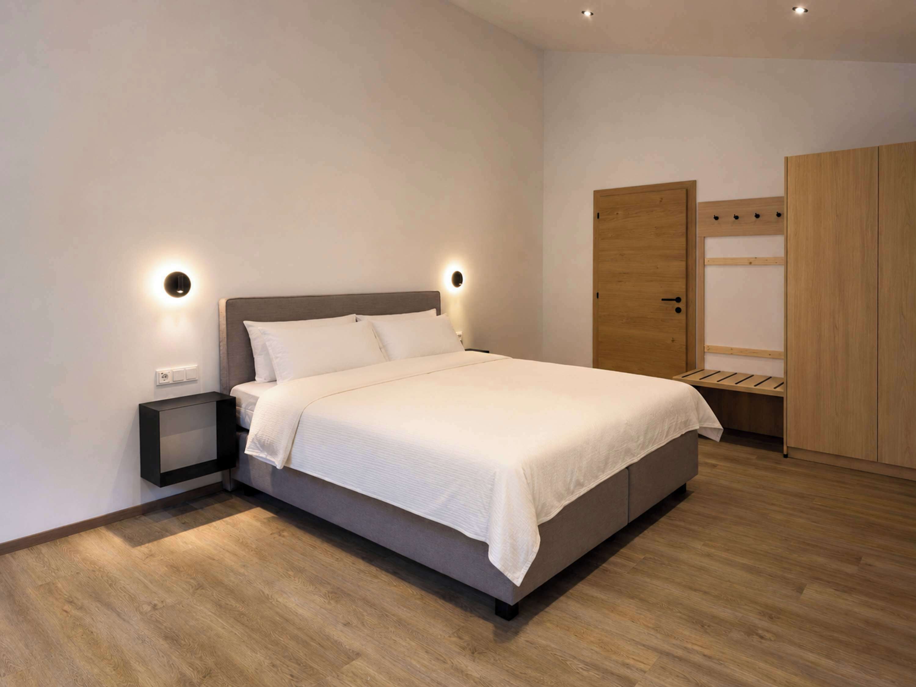 A modern bedroom with a large bed, bedside tables, a wardrobe, and built-in lighting.